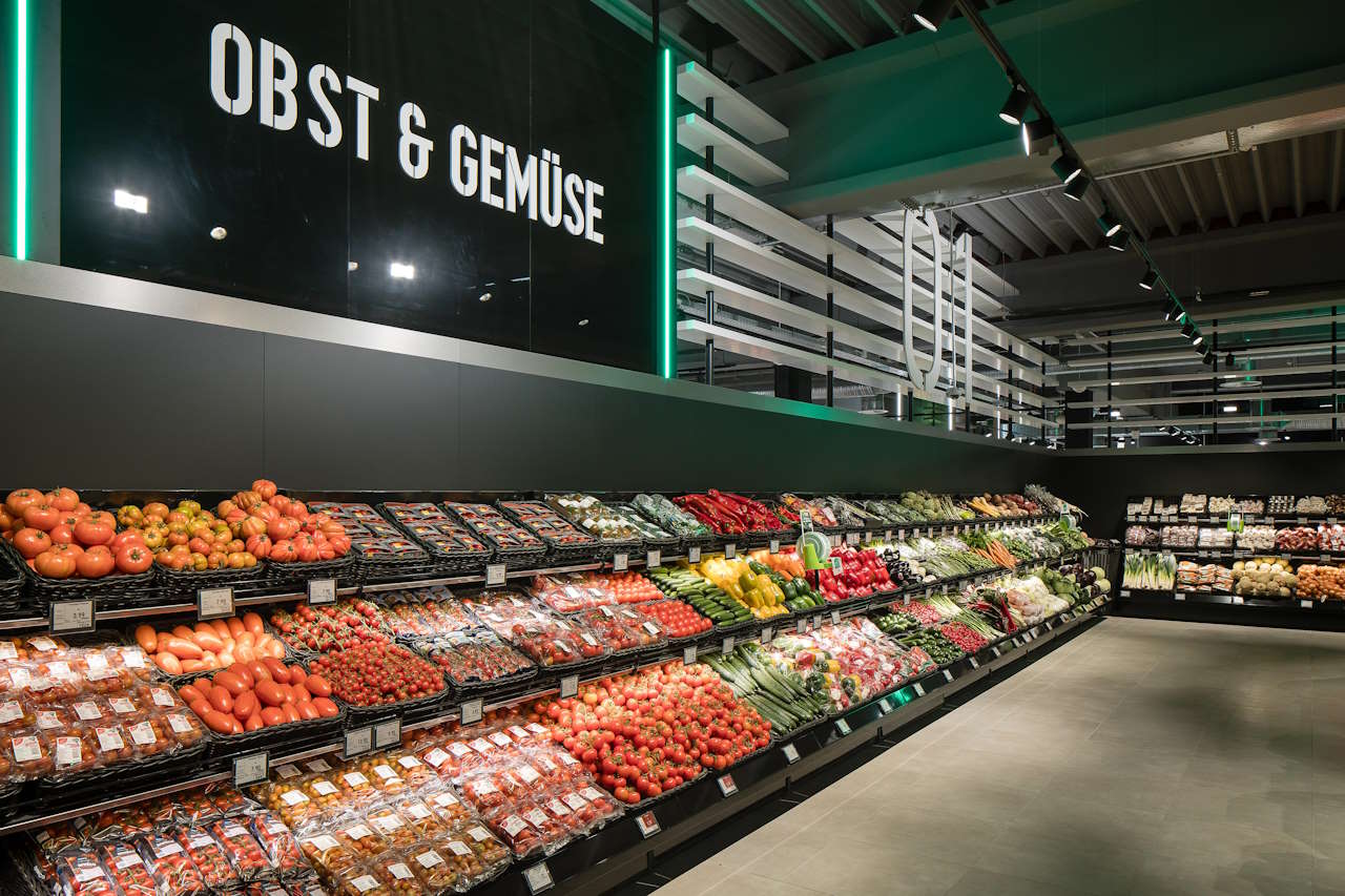 Supermarkt-Gemüseabteilung mit Regalen voller verschiedener frischer Tomaten, Paprika, Gurken und anderen Gemüsesorten unter einem Schild mit der Aufschrift "Obst & Gemüse".